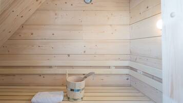 A wooden sauna with a bench, a bucket, and a towel.