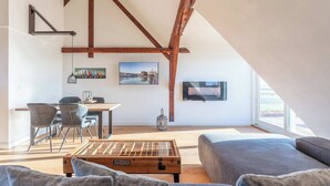 Um loft moderno com vigas de madeira expostas, área de jantar com mesa e cadeiras, uma janela grande e um espaço de estar aconchegante com um sofá.