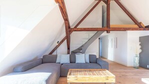 Um loft moderno com vigas de madeira aparentes, um sofá seccional cinza e uma mesa de centro de madeira.