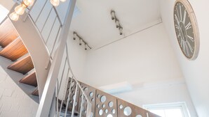 Um interior moderno com escada de madeira, relógio na parede e luminária no teto.