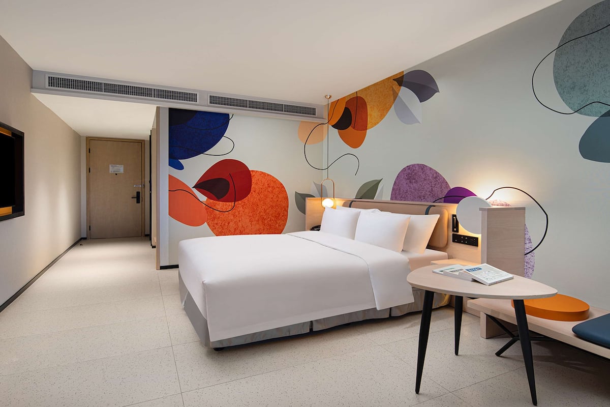 Une chambre d’hôtel moderne avec un grand lit, une table de chevet, une chaise et des œuvres d’art abstraites accrochées au mur.