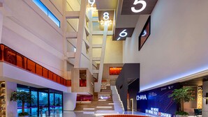 Un moderno vestíbulo de hotel con una zona de estar central, una escalera y una pared con pantalla digital.