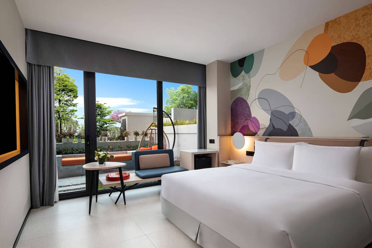 Une chambre d’hôtel moderne, dotée d’un grand lit, d’une petite table, d’une chaise et offrant une vue sur l’extérieur.