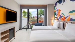 Una habitación de hotel moderna con una cama grande, un televisor de pantalla plana montado en la pared, una mesita con una silla y un balcón con vistas a la vegetación.