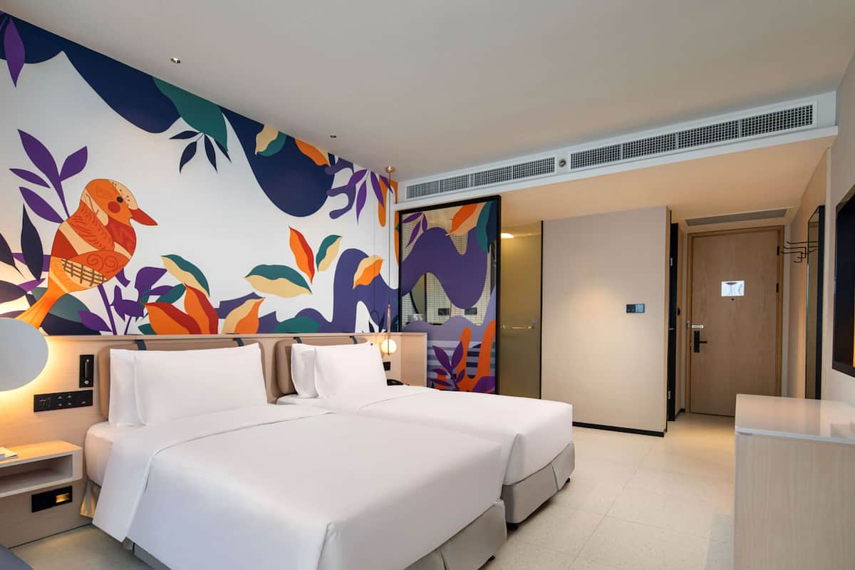 Une chambre d’hôtel moderne, dotée d’un grand lit, d’un bureau et d’une fresque murale abstraite aux couleurs vives.