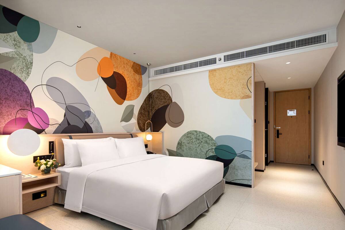 Une chambre d’hôtel moderne avec un grand lit, des tables de chevet, un bureau et un mur décoré d’œuvres d’art abstraites.