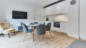 A modern kitchen with white cabinets, a built-in oven, and a wall-mounted clock. - Apartamenty Swinoujscie – Lissa (Swinoujscie)