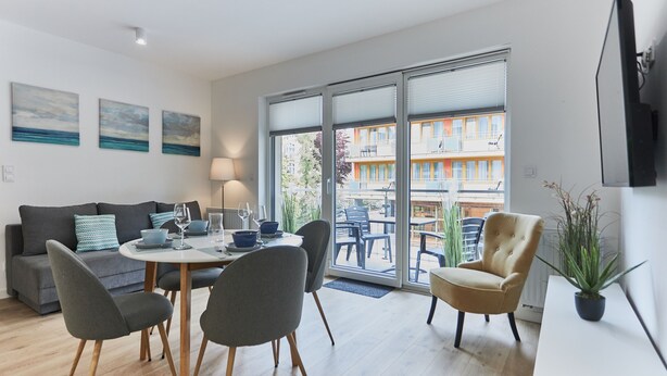 A modern living room with a sofa, dining table, chairs, and a TV. - Apartamenty Swinoujscie – Lissa (Swinoujscie)
