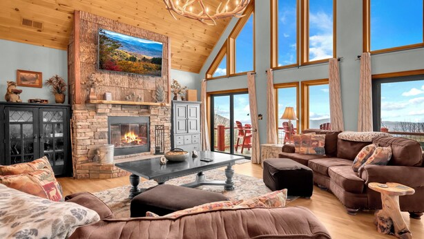 A spacious living room with a stone fireplace, large windows, and a high ceiling. - Upscale Home With Expansive Mountain Views (Banner Elk)