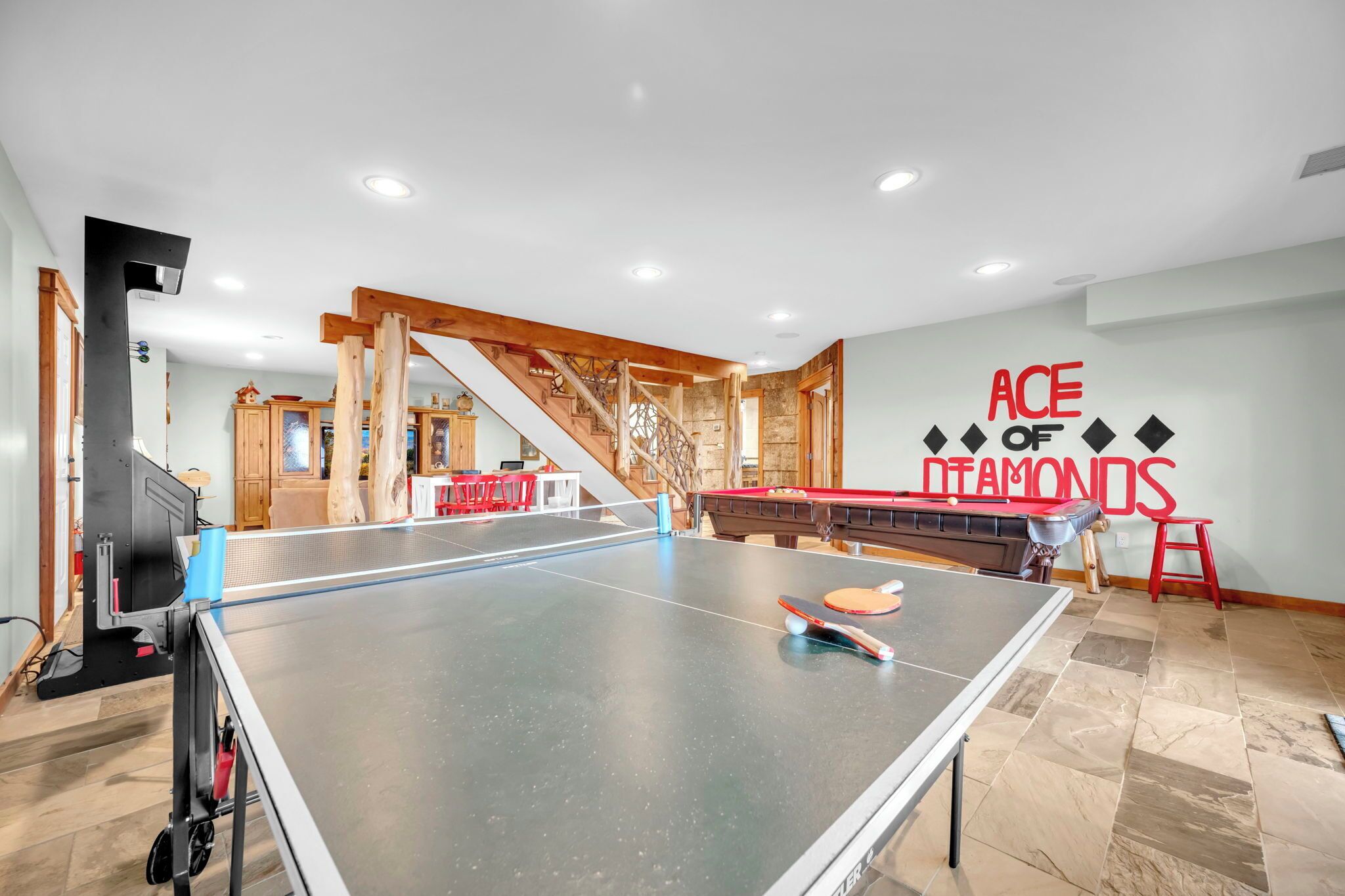 A ping pong table in a room with a pool table, wooden beams, and a staircase.