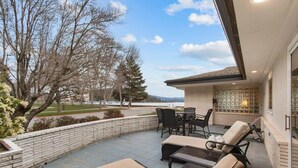 Une terrasse avec des meubles d’extérieur, un mur en briques et une vue sur des arbres et un paysage lointain.