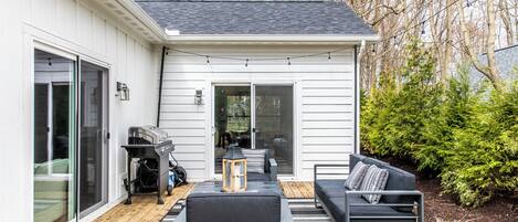 Un patio con mobiliario exterior, una parrilla y una puerta corrediza que da a una terraza.