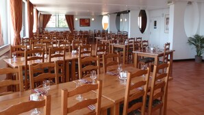 A spacious dining area with multiple wooden tables and chairs, large windows with curtains, and a potted plant. - La Vallée Blanche (Huez)
