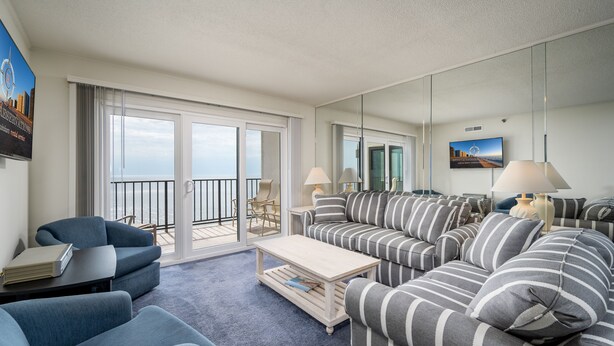 Un salon moderne avec un grand canapé, des fauteuils, une table basse et un balcon offrant une vue agréable.