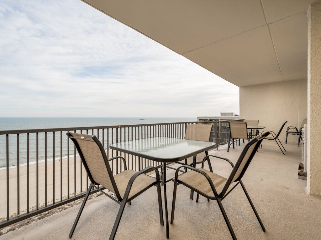 A balcony with a glass table and chairs, overlooking a beach.