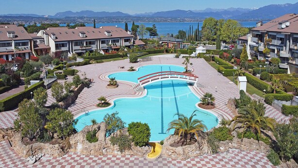 Ein Resort mit einem zentral gelegenen Schwimmbad, mehreren Gebäuden und einer Bergkulisse.