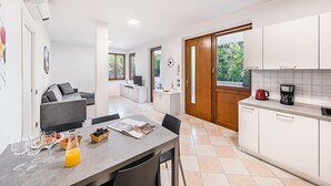Eine moderne Küche mit weißen Schränken, ein Essbereich mit Tisch für Zwei und eine Wohnfläche mit grauem Sofa.