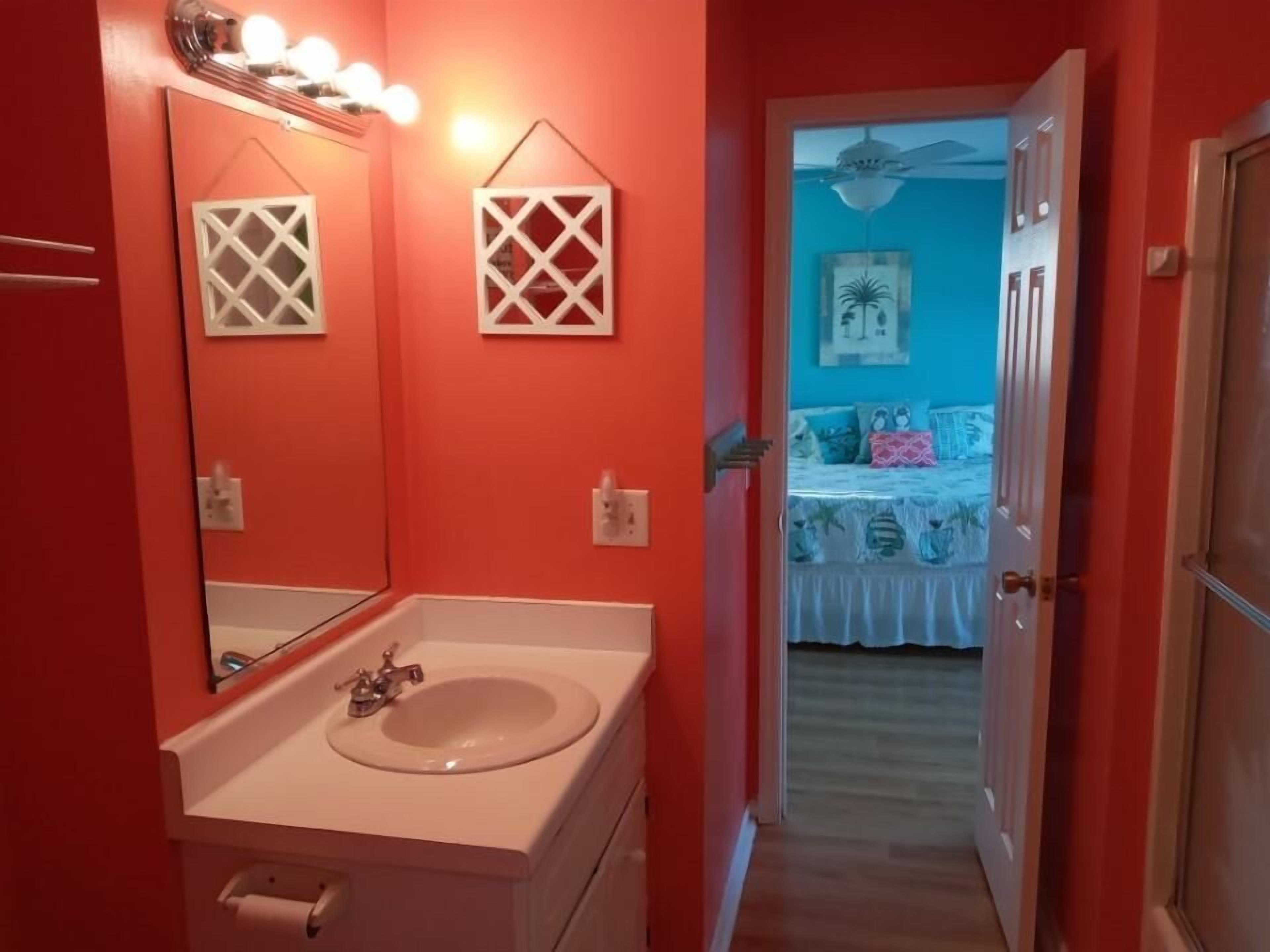 Un baño con lavamanos blanco, espejo y pared roja.