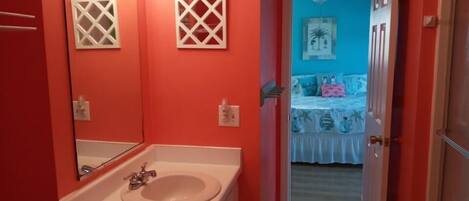 Un baño con lavamanos blanco, espejo y pared roja.