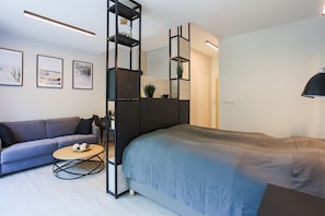A modern bedroom with a bed, a sofa, a coffee table, and a bookshelf. - Apartamenty Swinoujscie – Cesarskie Ogrody (Swinoujscie)