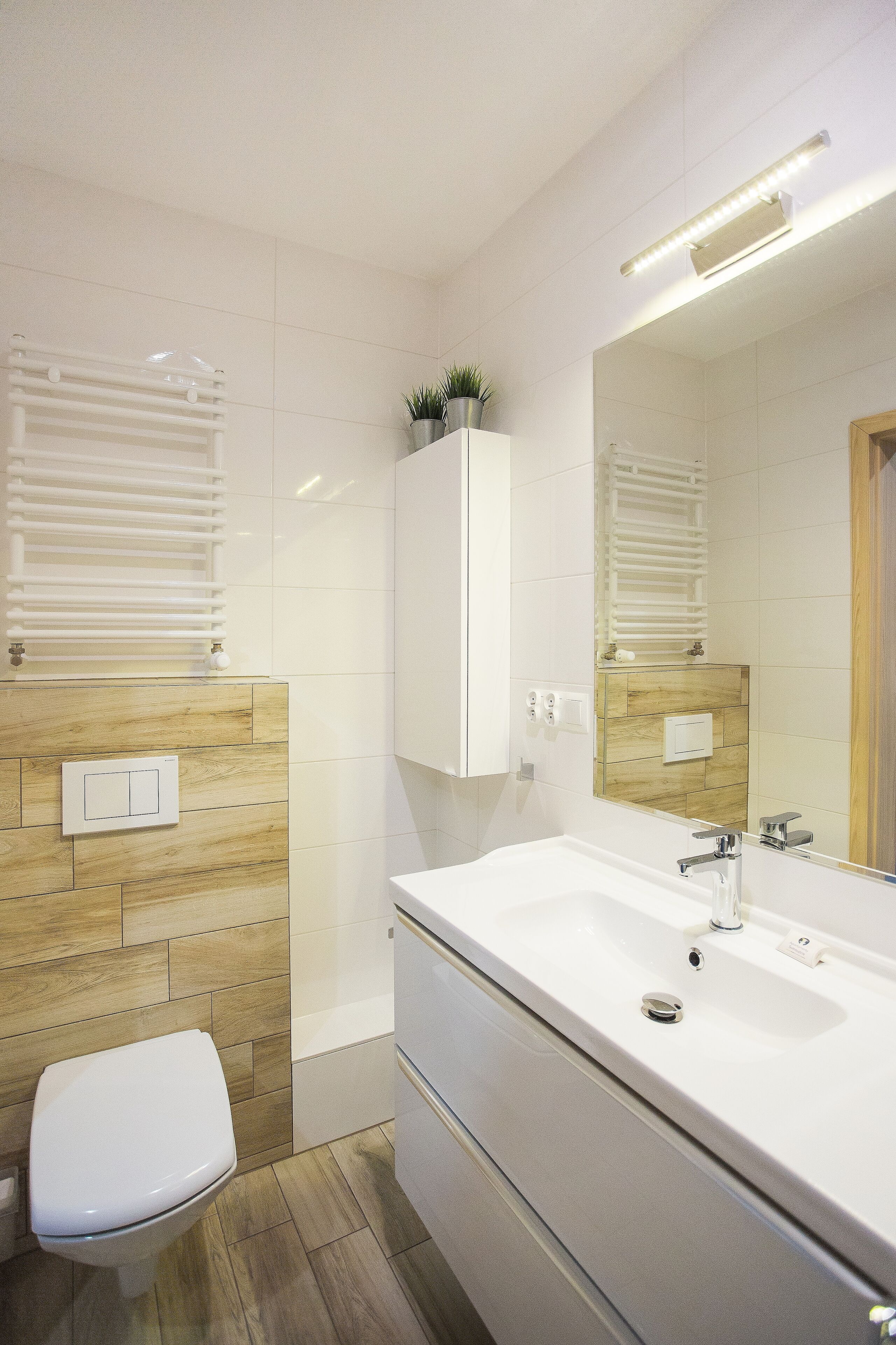 A modern bathroom with a white toilet, a large sink with a mirror, and a towel rack.