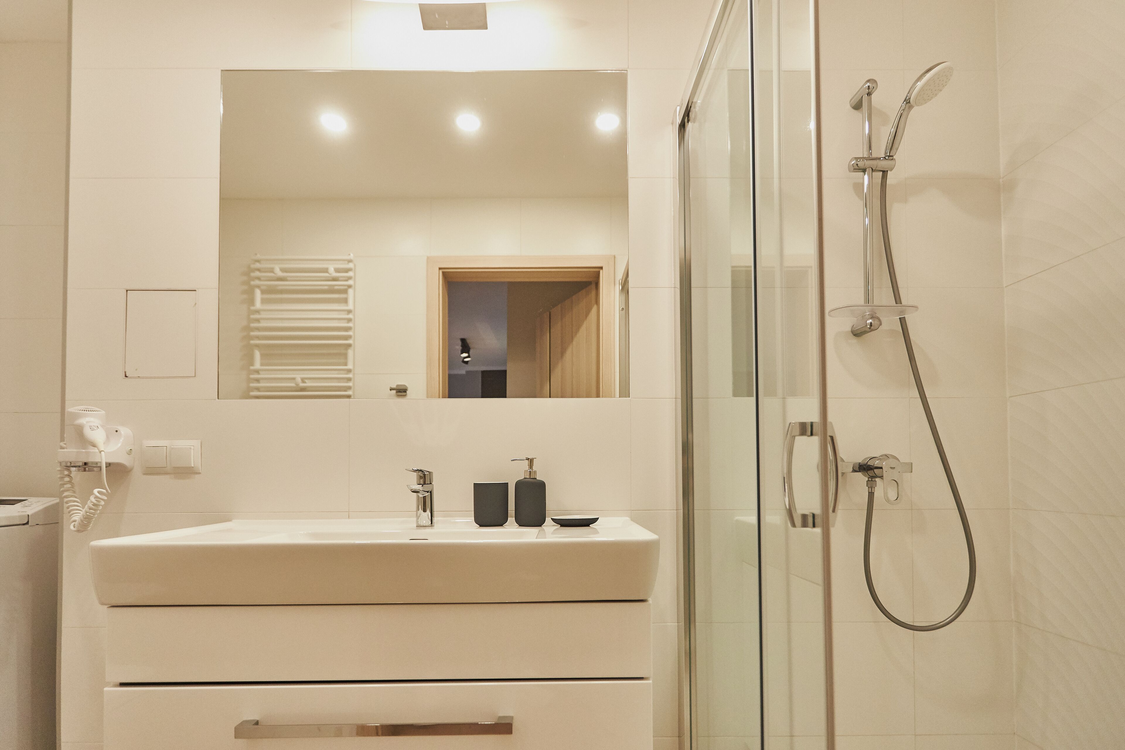Un baño moderno con cabina de ducha de vidrio, un lavamanos blanco con espejo y un perchero para toallas.