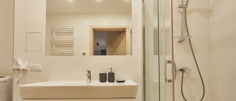 Un baño moderno con cabina de ducha de vidrio, un lavamanos blanco con espejo y un perchero para toallas.