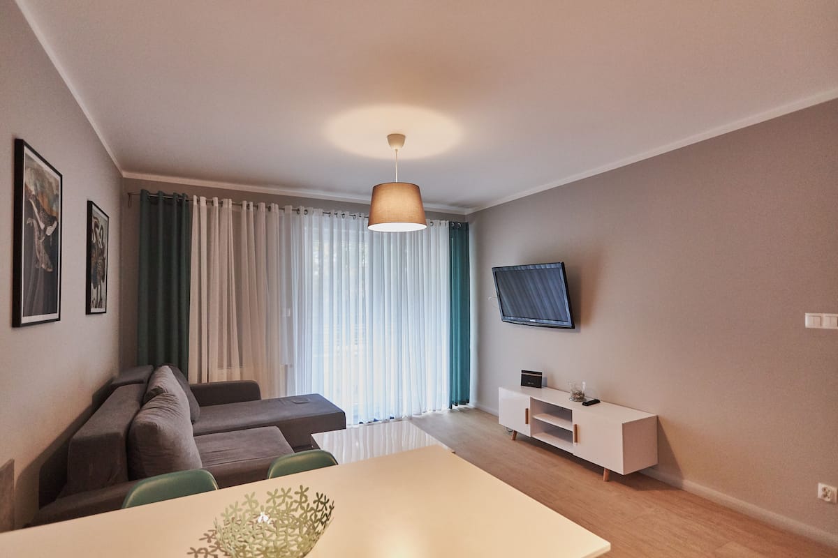 Ein modernes Wohnzimmer mit einer Couch, einem Esstisch und einem an der Wand montierten Fernseher.