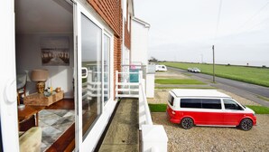 A residential property with a sliding glass door leading to a balcony, a white van parked outside, and a view of a road and greenery. - Sea Breeze, Selsey -  a town house that sleeps 6 guests  in 3 bedrooms (Chichester)