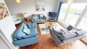 A modern living room with a large TV, grey sofas, and a wooden herringbone floor. - Sea Breeze, Selsey -  a town house that sleeps 6 guests  in 3 bedrooms (Chichester)