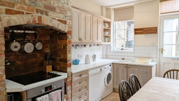 Une cuisine avec un mur en briques, des meubles en bois, un lave-linge et un coin repas avec des chaises.