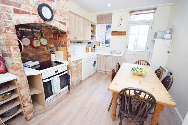 A kitchen with a brick oven, wooden cabinets, a dining table with chairs, and a window with curtains.