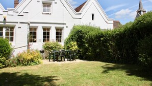 Une maison blanche à deux étages, avec un jardin et une petite table et des chaises dans le jardin avant.