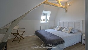 Un dormitorio con techo inclinado, una cama con ropa de cama a rayas, una ventana con vistas y una silla de madera.