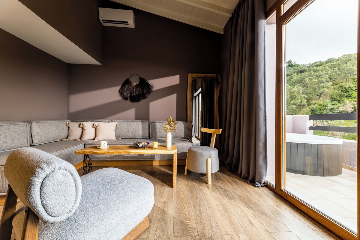 A modern living room with a sofa, a coffee table, and a chair. There is a large window with curtains, and a view of a balcony.
