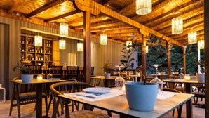 A restaurant with wooden tables and chairs, hanging lights, and a bar area with shelves of bottles. - Avaton Suites & Villa Philian Collection (Skiathos)