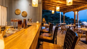 An outdoor dining area with wooden tables and chairs, hanging lights, and a view of trees at dusk. - Avaton Suites & Villa Philian Collection (Skiathos)