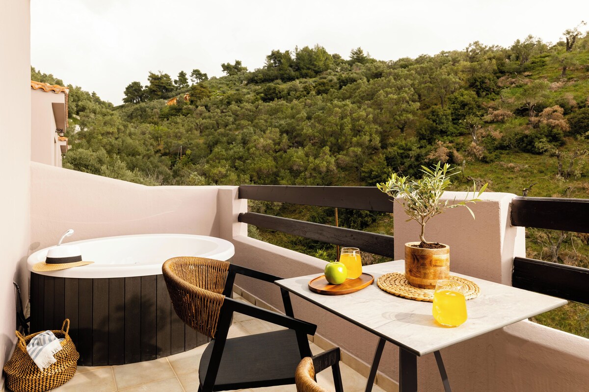A balcony with a hot tub, wicker chairs, a table with a plant, a basket, and a glass of orange juice.