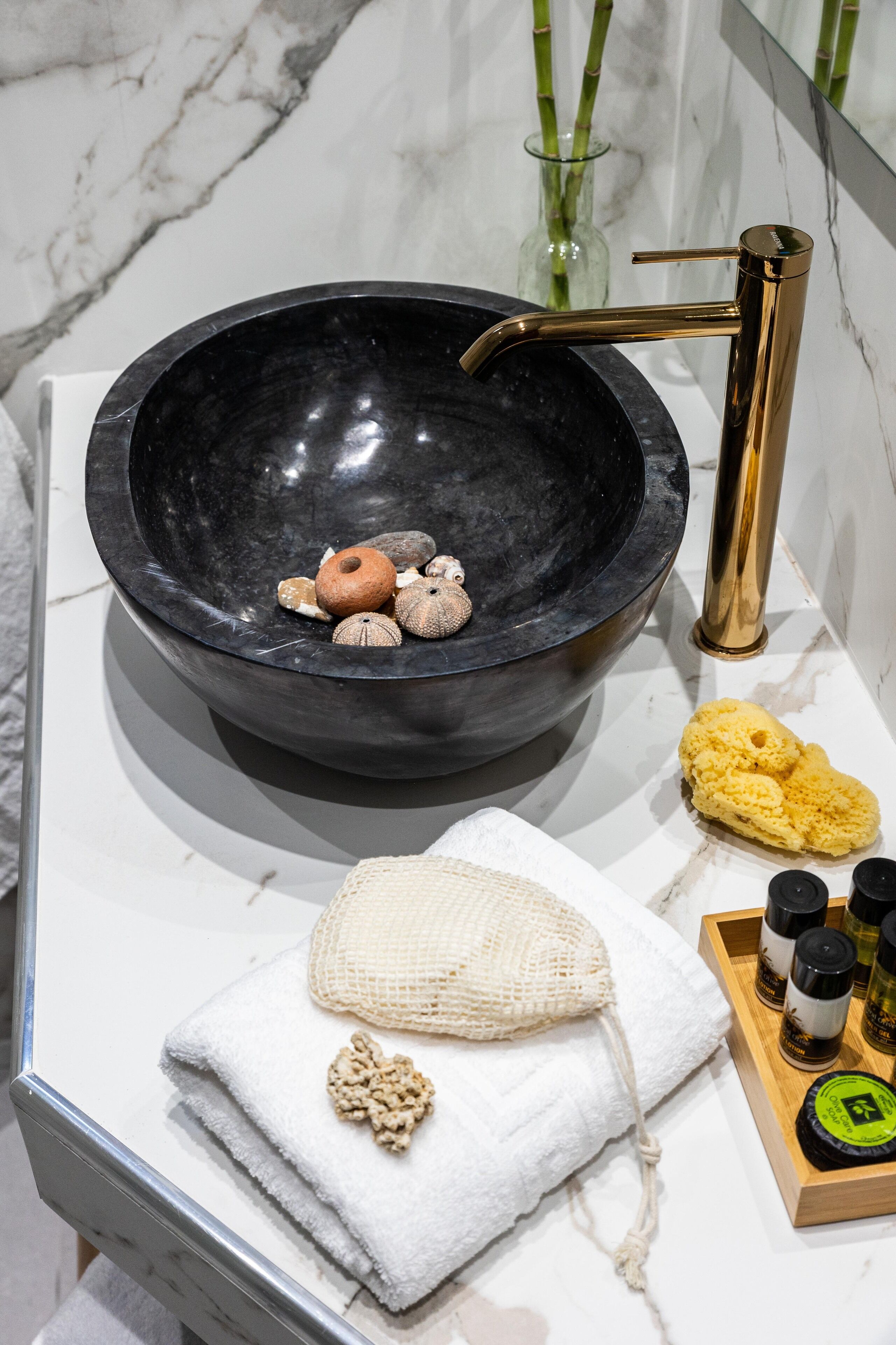 A bathroom with a black basin, gold faucet, and various toiletries on the counter.