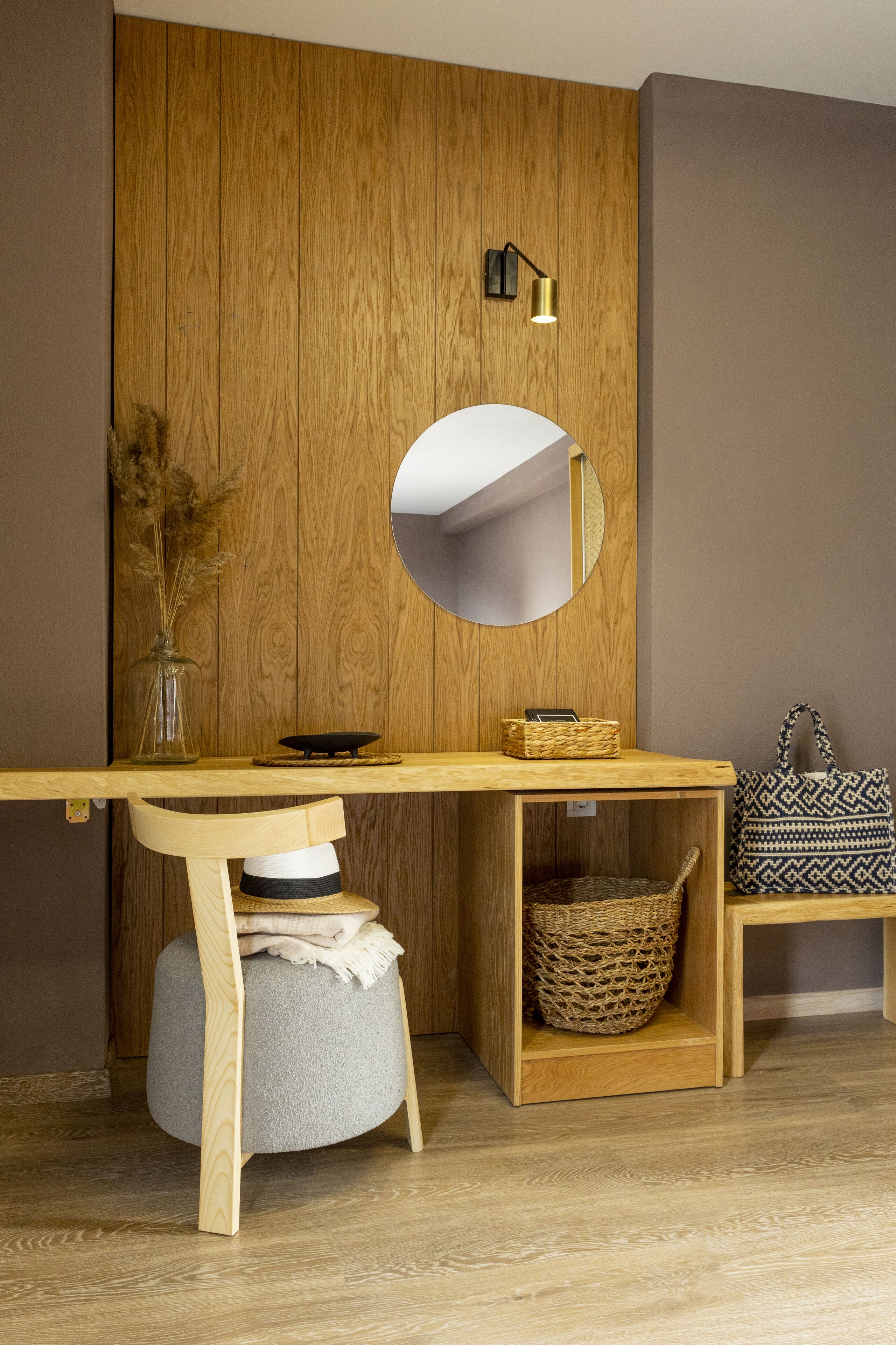 A wooden desk with a mirror, a wicker basket, and a grey ottoman.