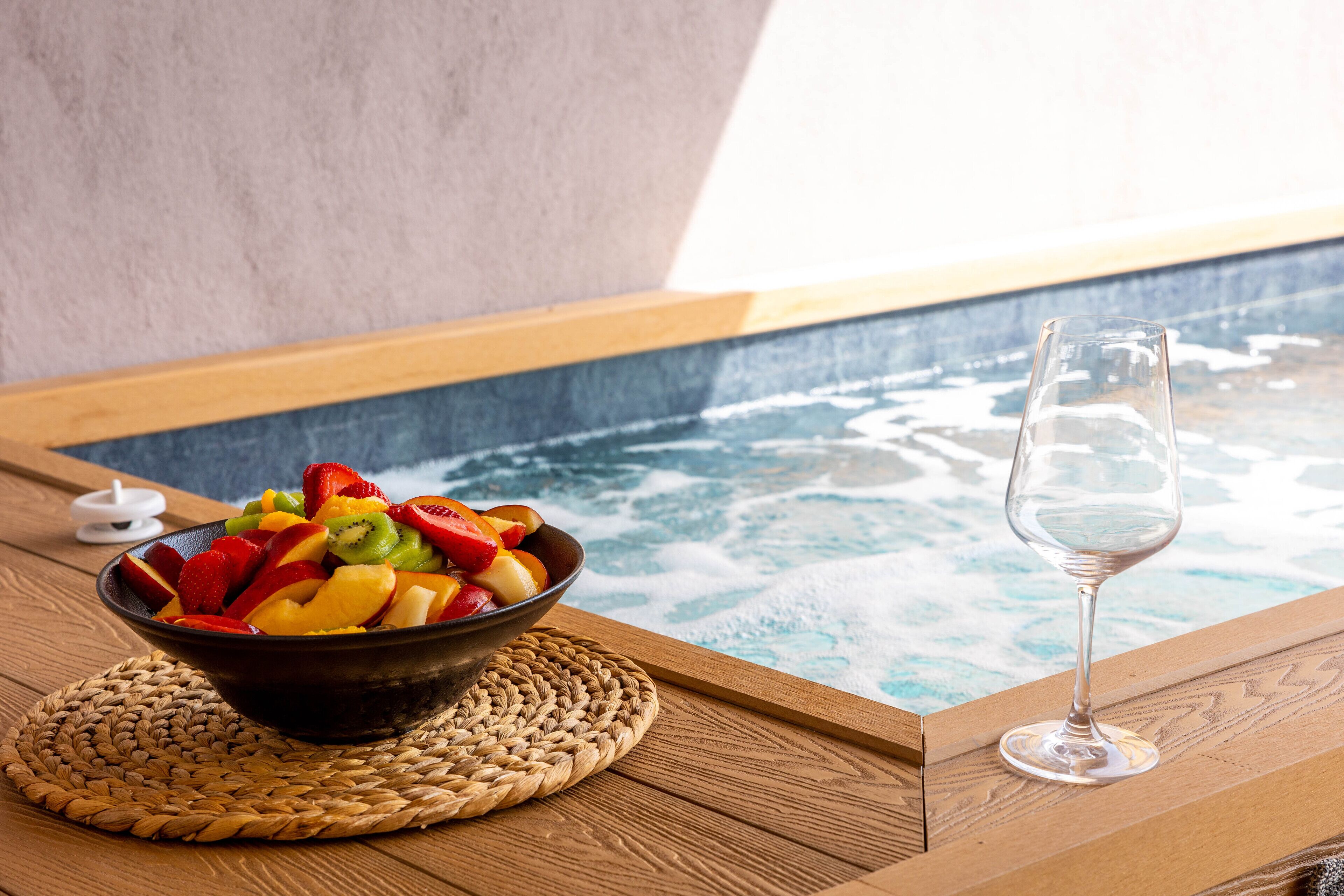 Ein Holztisch mit Obstschale und einem Glas Wasser in der Nähe eines Whirlpools.