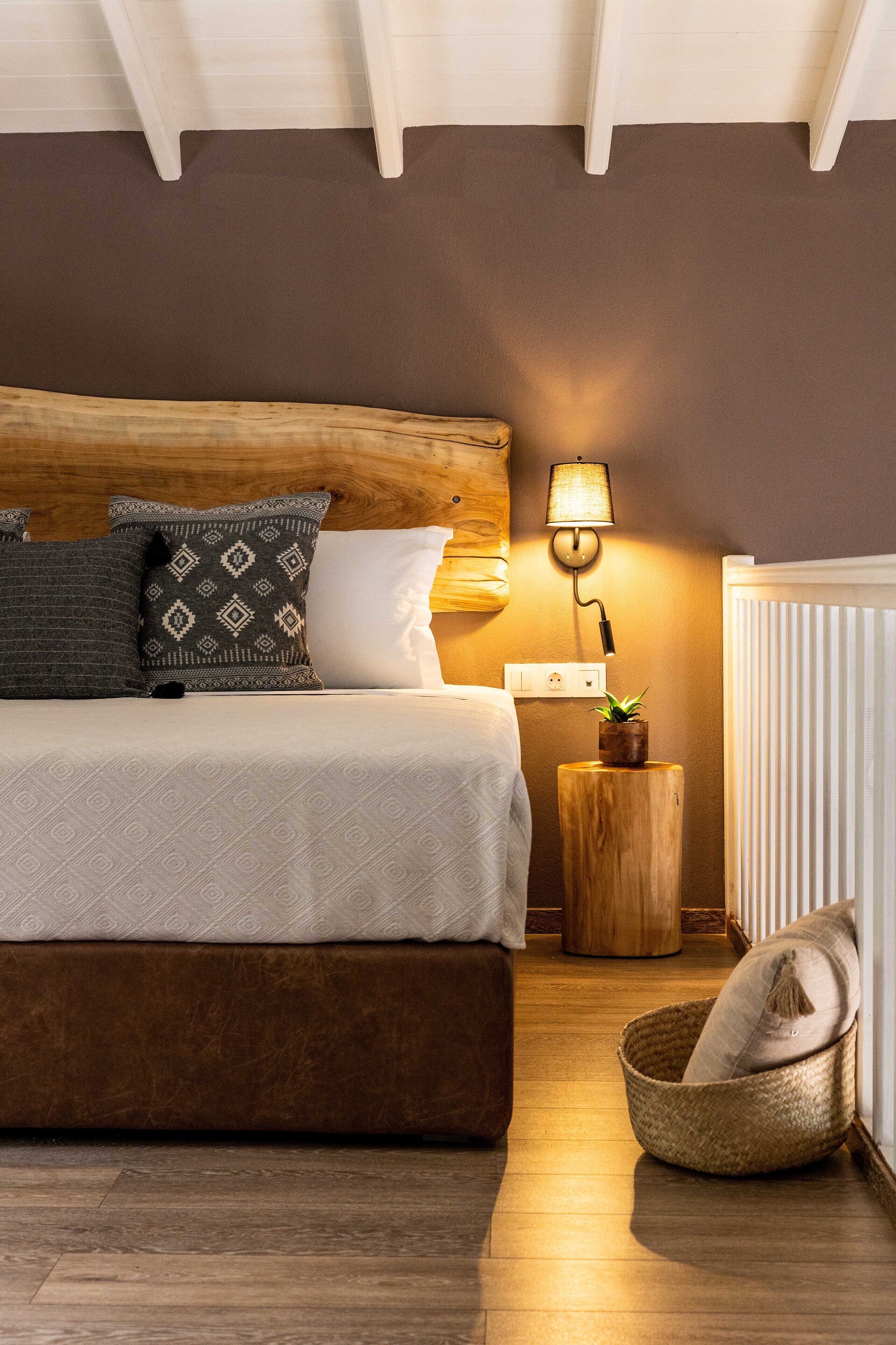 A bedroom with a wooden headboard, a bedside lamp, a small wooden nightstand, and a wicker basket.