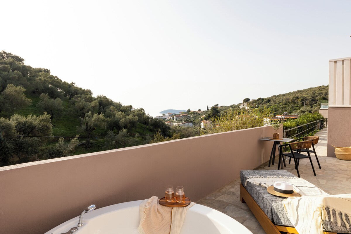 A balcony with a bathtub, two glasses of drink, a hat, and a table with chairs.