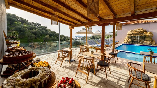 A terrace with wooden furniture, a pool, and a view of the landscape. - Avaton Suites & Villa Philian Collection (Skiathos)