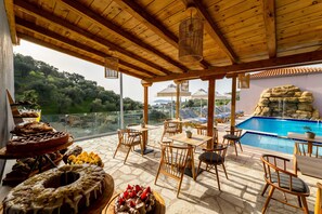 A terrace with wooden furniture, a pool, and a view of the landscape. - Avaton Suites & Villa Philian Collection (Skiathos)