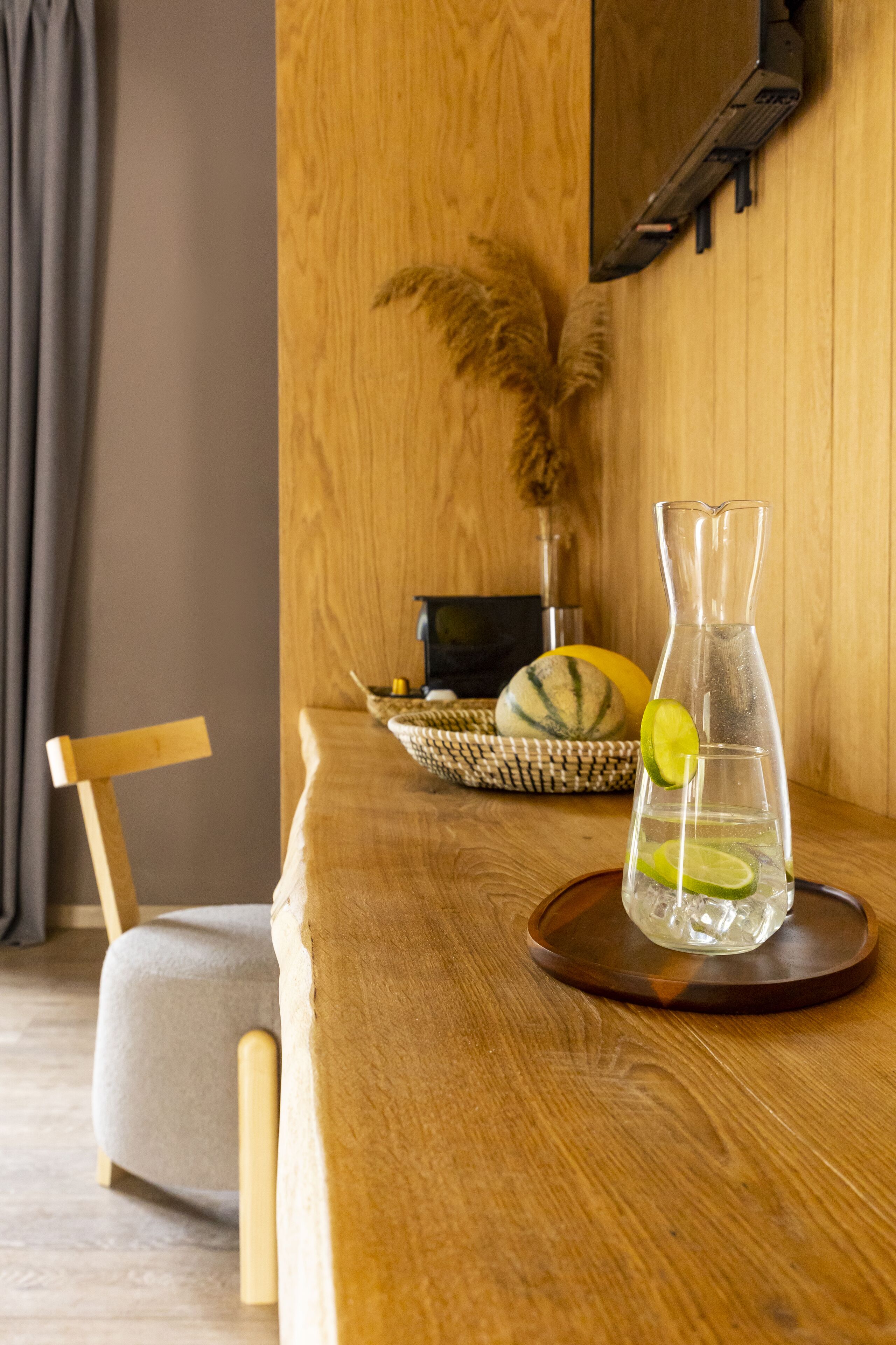 A wooden table with a clear glass decanter, a slice of lime, and a woven basket containing a melon and a bottle.