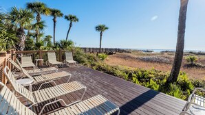 A wooden deck with lounge chairs, palm trees, and a view of the beach.