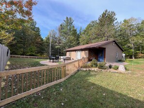 A small cabin with a deck, surrounded by a wooden fence, and a grassy yard.