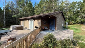 Une petite cabane avec une terrasse, un espace extérieur couvert aménagé en coin salon et un garage.