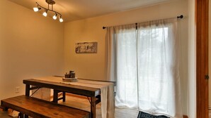 Une pièce avec une table et un banc en bois, un luminaire au plafond, une fenêtre avec des rideaux et un paillasson.